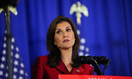 Woman in red dress speaks in front of a flag