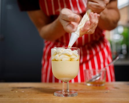 Whipped cream being added to a glass of flummery