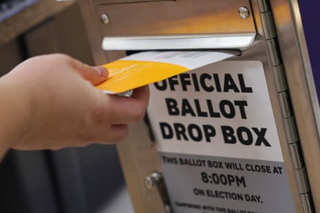 A hand places a ballot into an official ballot drop box during early voting
