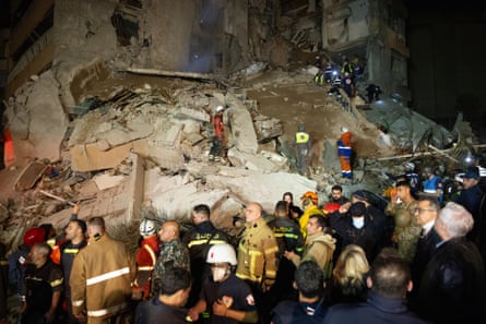 Dozens of people at destroyed building lit up at night