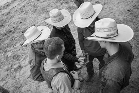 Above position of 5 men look astatine a phone, 4 of them wearing cowboy hats