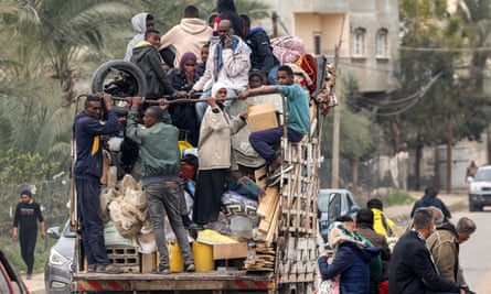 People ride in the back of a truck with belongings as they flee from Rafah