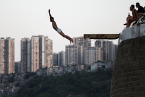 A man dives into a river, which is out of shot, with high-rise apartment buildings in the background