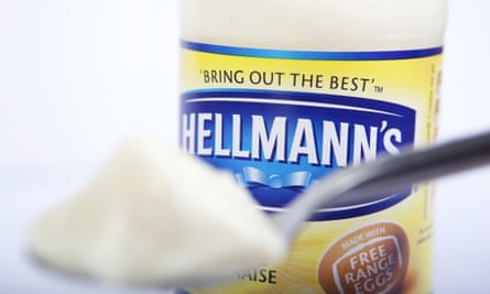 A close-up of a spoonful of mayonnaise, with a bottle of Hellmann’s in the background.