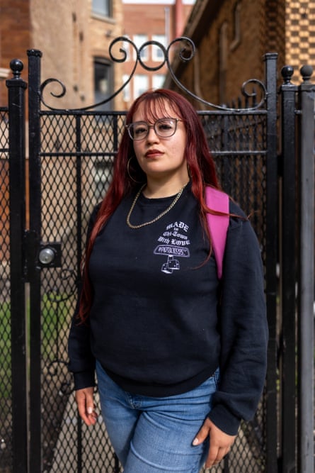 A woman with red hair and glasses stands for a portrait in front of an iron gate