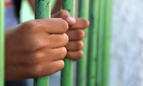Hands of a young boy holding prison bars