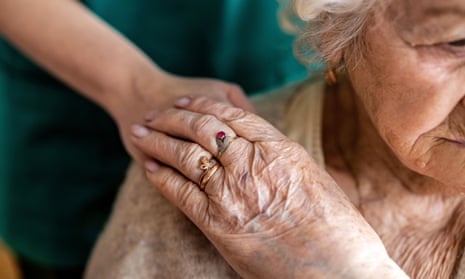 An elderly woman holds hands with a carer