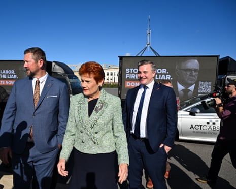 One Nation leader Pauline Hanson speaks to the media as billboard trucks drive past Parliament House.