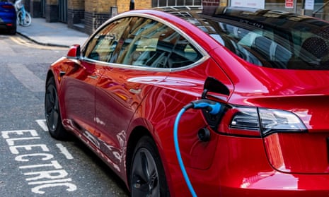 A red Tesla Model 3 in an electric car charging bay on a street, plugged in