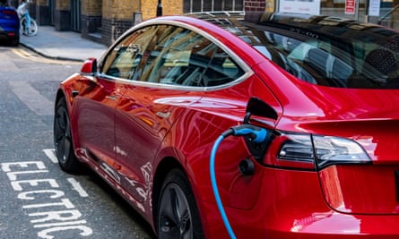 A red Tesla Model 3 parked and charging on city street