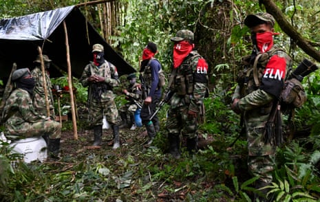 Seven men in camouflage outfits, caps and “ELN” badges at a tent in a forest
