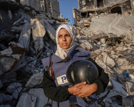 Mariam Dagga fotografiada con un chaleco antibalas y sosteniendo un casco frente a edificios destruidos.