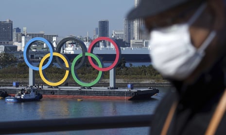 A man wearing a face mask with the Olympic rings in the background in Tokyo