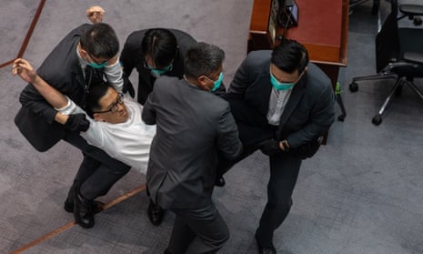 A pro-democracy lawmaker is carried out of the chamber by security guards during a scuffle with pro-Beijing lawmakers at a the legislative council meeting in Hong Kong