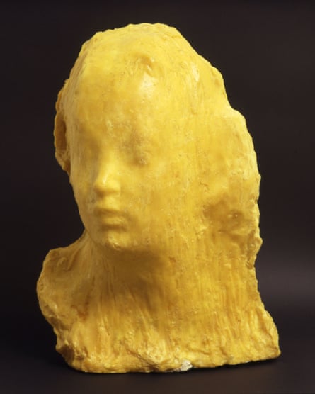 A sculpture of a human head that looks as if it’s melting, in a browny-yellow colour.