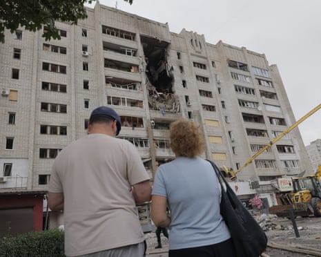 Two residents stand viewing a severely damaged multi-story residential building in Kharkiv