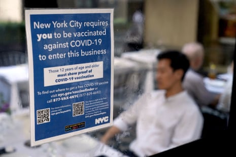 A blue sign in the window of a restaurant in Manhattan explains that proof of vaccination is required for indoor dining. Inside, diners can be seen eating at tables.