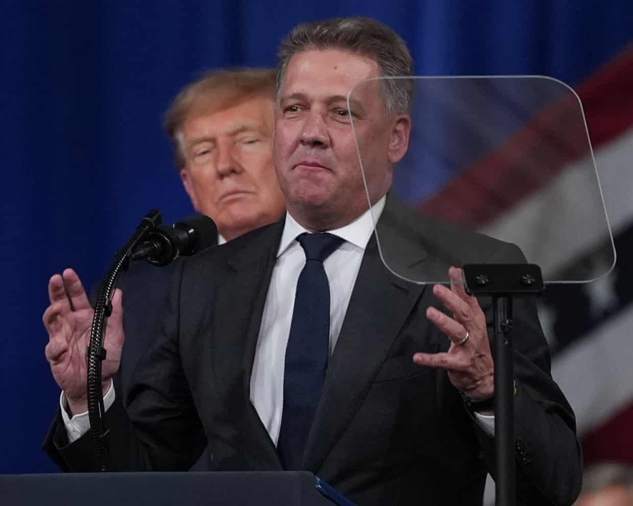Trump watches from behind as Döllner speaks at a lectern
