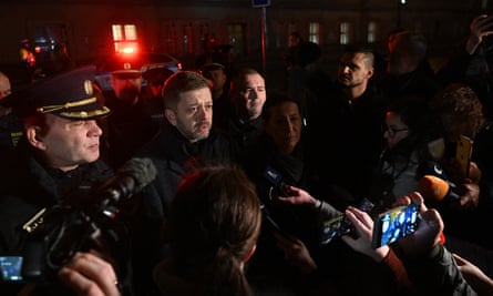 A group of men some in uniform, gathered t give a press conference in front of a collection of microphones