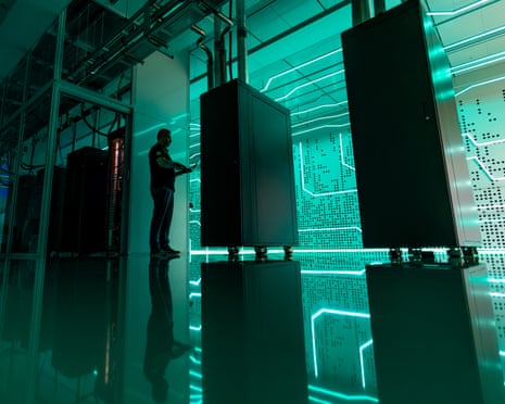 A technician checks liquid-cooled server racks in a glowing teal-lit datacentre