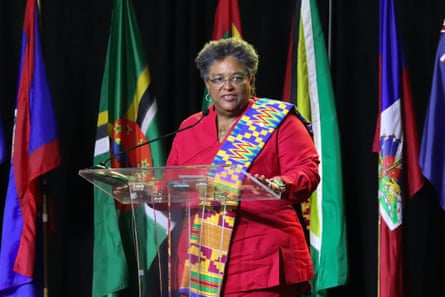 Mottley stands at a lectern in front of various Caribbean flags