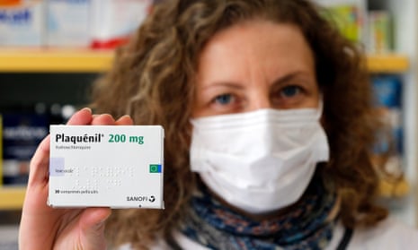 A pharmacy employee in France wearing a protective mask shows a box of hydroxychloroquine.