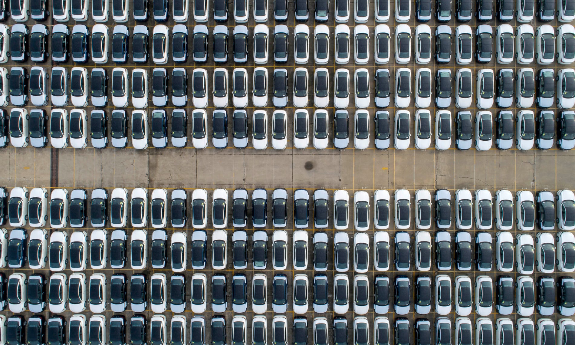 an overhead shot of a huge number of new cars parked in rows