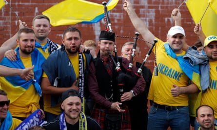 Ukraine fans with national flags pose with a man playing the bagpipes