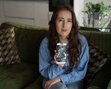 Meg is sitting connected a greenish velvet sofa holding up a achromatic and achromatic image of Eve connected her telephone from erstwhile she had cancer