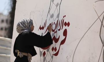 A Palestinian woman writes slogan over a map of Israel painted with an Arab keffiyeh imposed over it.