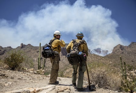 In June, firefighters talk near the Finger Rock Canyon trailhead as smoke billows from the Bighorn Fire in the distance, in Tucson, Arizona.