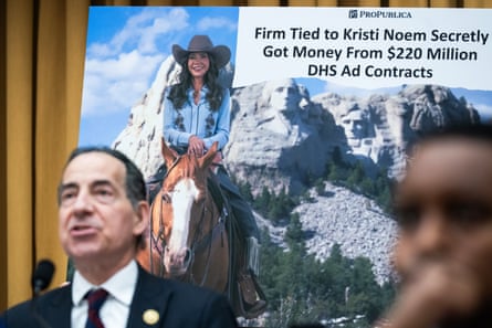 a man speaks in front of a placard titled ‘firm tied to Kristi Noem secretly got $220 million DHS aid contracts’