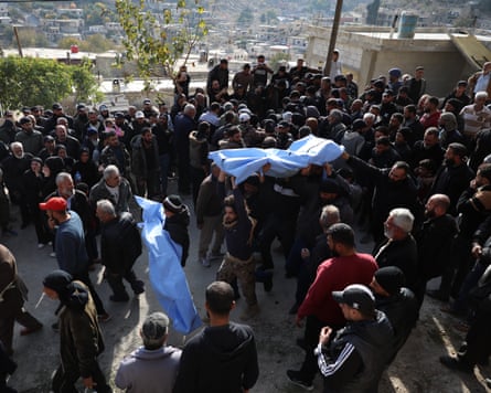 People carry bodies wrapped in shrouds through a crowd at funeral ceremony