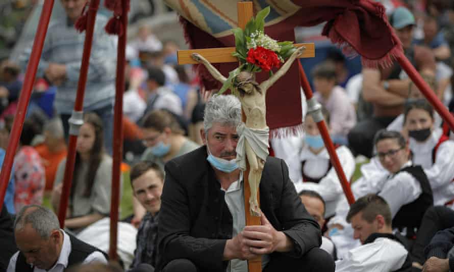 A man holds a crucifix as Catholic pilgrims fill the hillsides.