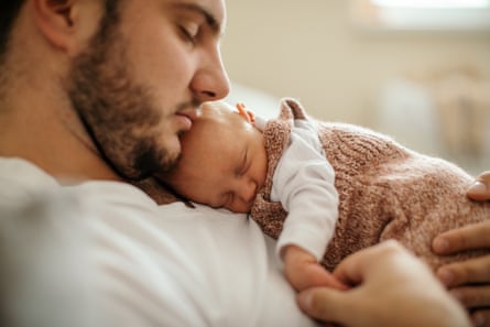 A baby sleeping in her father’s arms at their home.