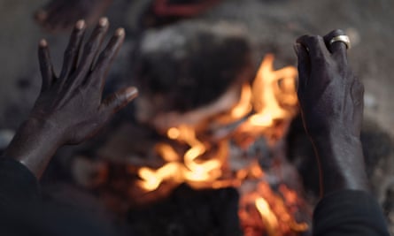 A worker warms his hands over a fire as night falls at the migrant camp in Campobello di Mazara.