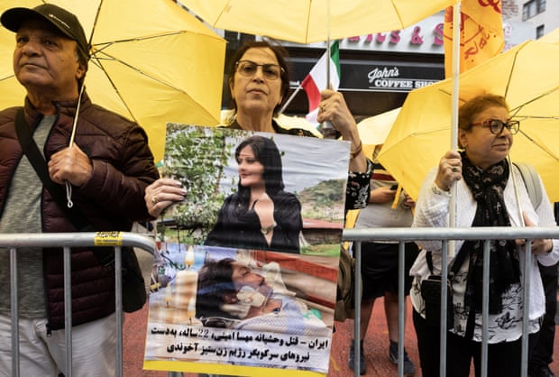 A woman holds a poster showing two portraits of a young woman. In the photo below, the woman is in a hospital bed.
