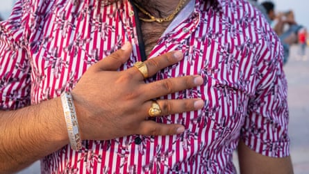تصویر نزدیک از کارگر مهاجر در قطر در اوقات فراغت خود با پیراهن راه راه قرمز و سفید و جواهرات طلا روی انگشتانش.