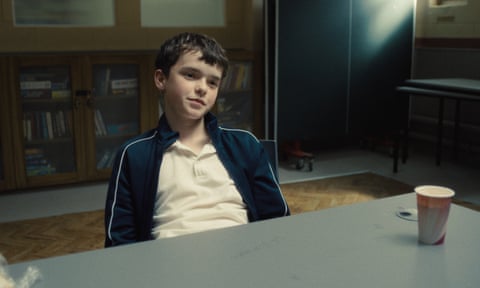 Owen Cooper sitting at a table in a secure room as 13-year-old Jamie Miller in the Netflix drama Adolescence.