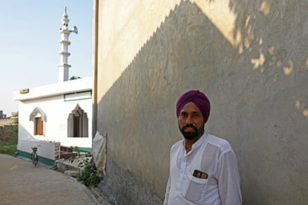 Jaspal Sharma stands by a wall, with a white mosque and minaret behind him