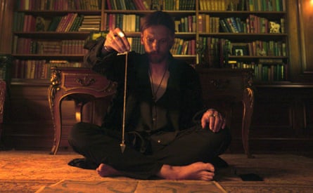 Jamie Campbell Bower as Alexander Babtiste sits cross-legged on the floor holding a pendulum in Witchboard.