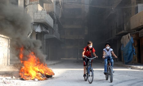 Syrian children cycle past tyres in Aleppo.