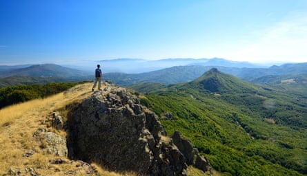 A sole figure on top of a peak gazes into a mountainous landscape