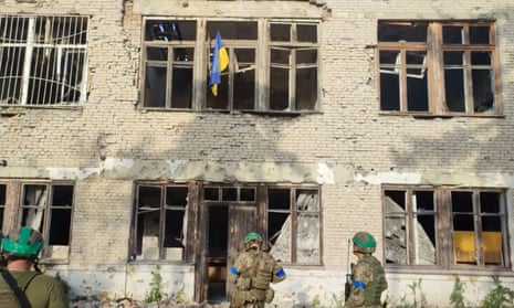 Ukrainian soldiers stand in front of a building flying a Ukrainian flag during an operation that claims to have liberate the first village of their counteroffensive