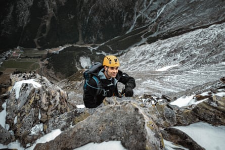 A man in a climbing hard hat ascends a steep rocky path.