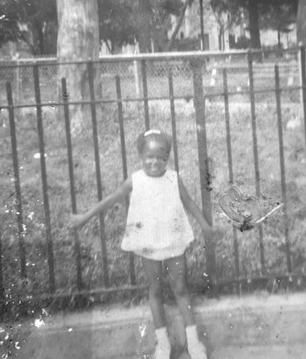 A young Katrina Brownlee poses against some railings in a white dress with white socks.