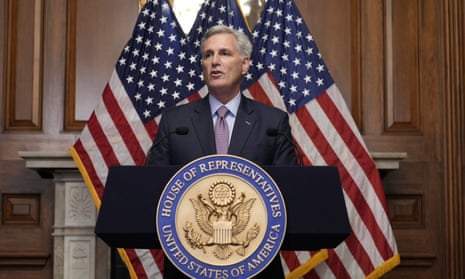 Kevin McCarthy, in a navy suit, stands behind a podium and in front of three American flags. 