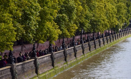 Queue of people along the river and next to the Covid memorial wall with trees above it