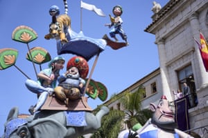 Spain's King Felipe and Queen Letizia stand on a balcony as oversized cartoon characters pass by