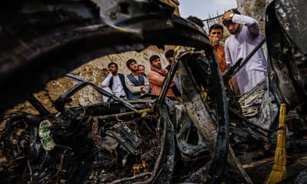People gather round a car destroyed by a US drone strike